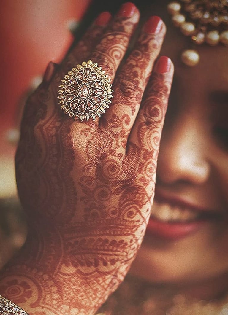 Bride showing her Mehandi with one eye closed using her hand