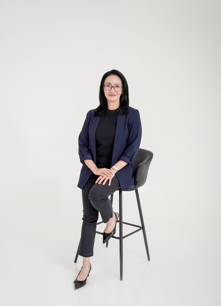 Professional woman in a navy blazer and glasses sitting on a bar stool for a business portrait.