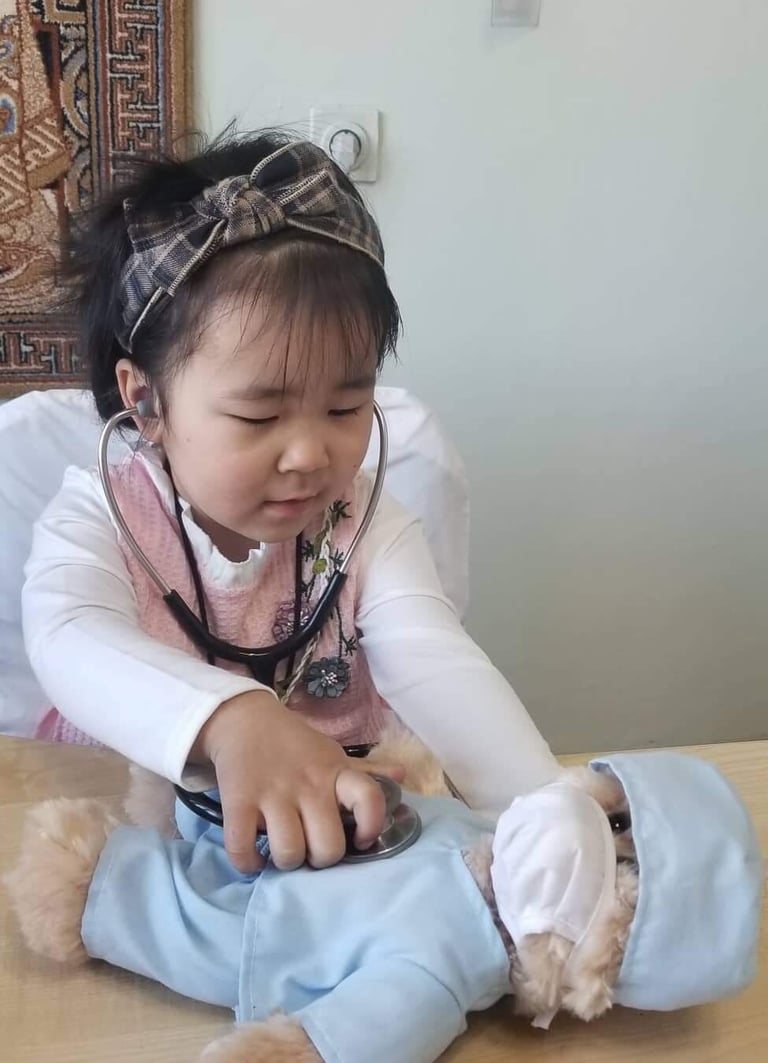 a little girl in a pink dress playing doctor to a teddy bear