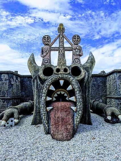 Mystical stone monster sculpture by Rober Tatin with a large open mouth and carved tribal figures