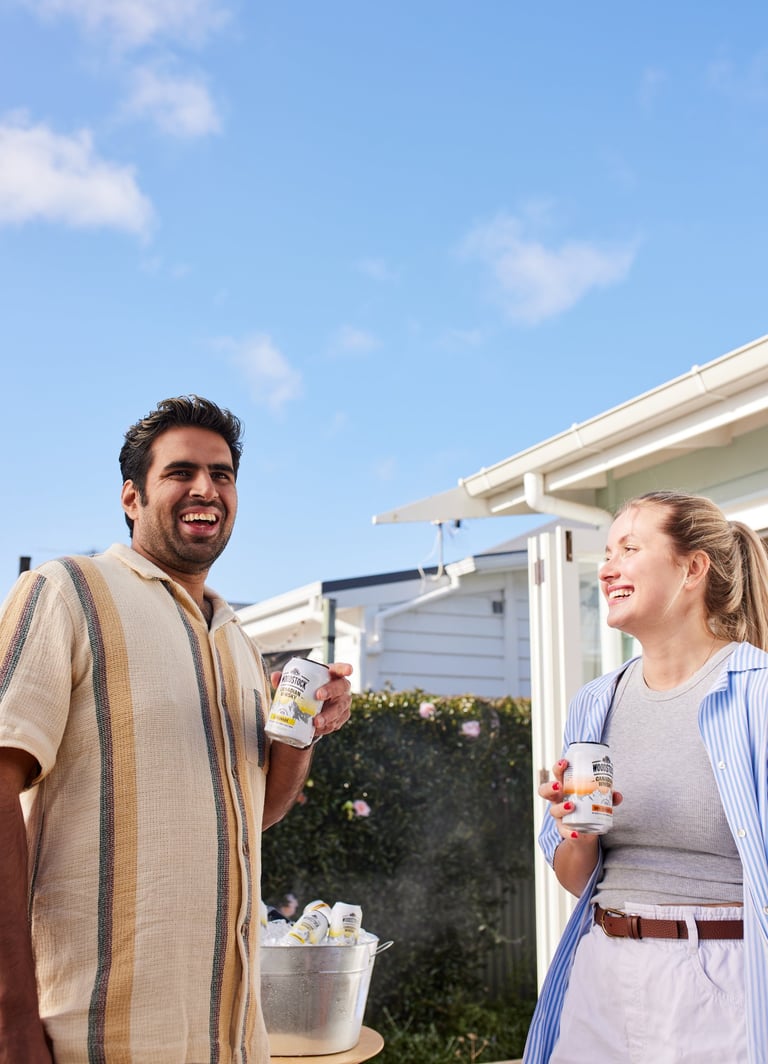Product campaign photography - a man and woman standing outside of a house holding woodstock cans