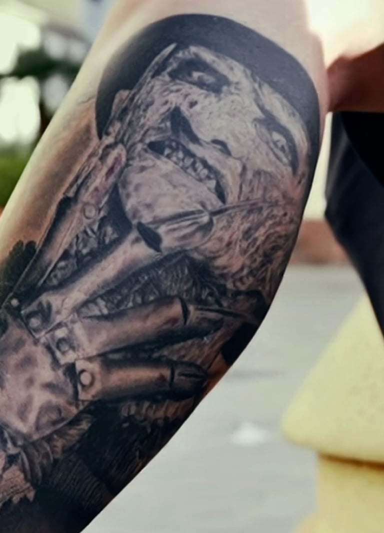 Realistic black and grey Freddy Krueger tattoo on an arm featuring his iconic bladed glove and burnt face.