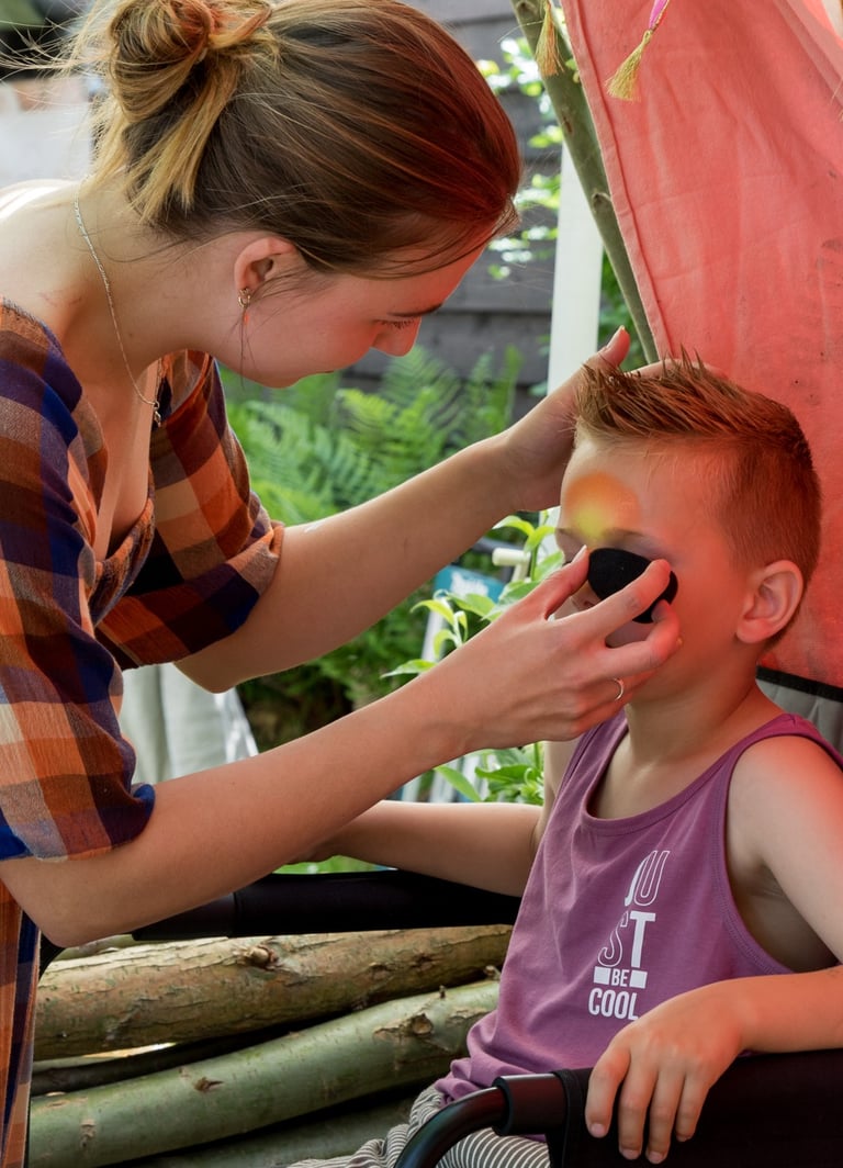 Een jongetje krijgt geconcentreerd een stoer oogmasker geschminkt met een sponsje.