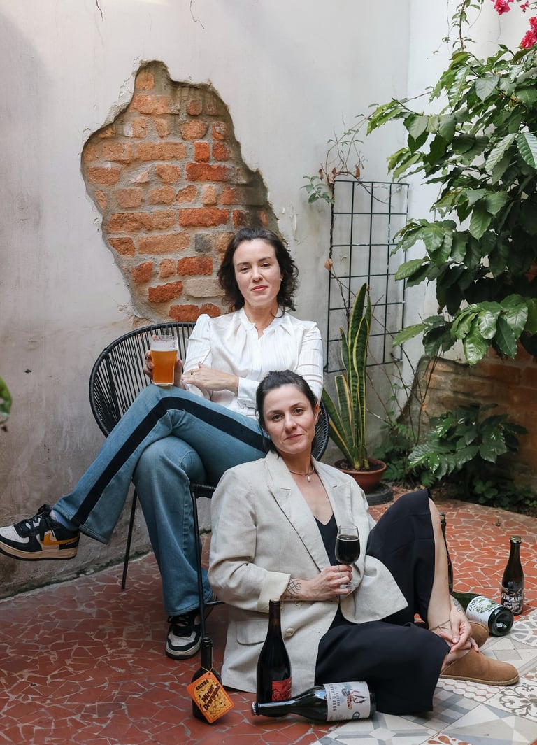 Two women enjoying craft beer and wine in a rustic outdoor patio with exposed brick.