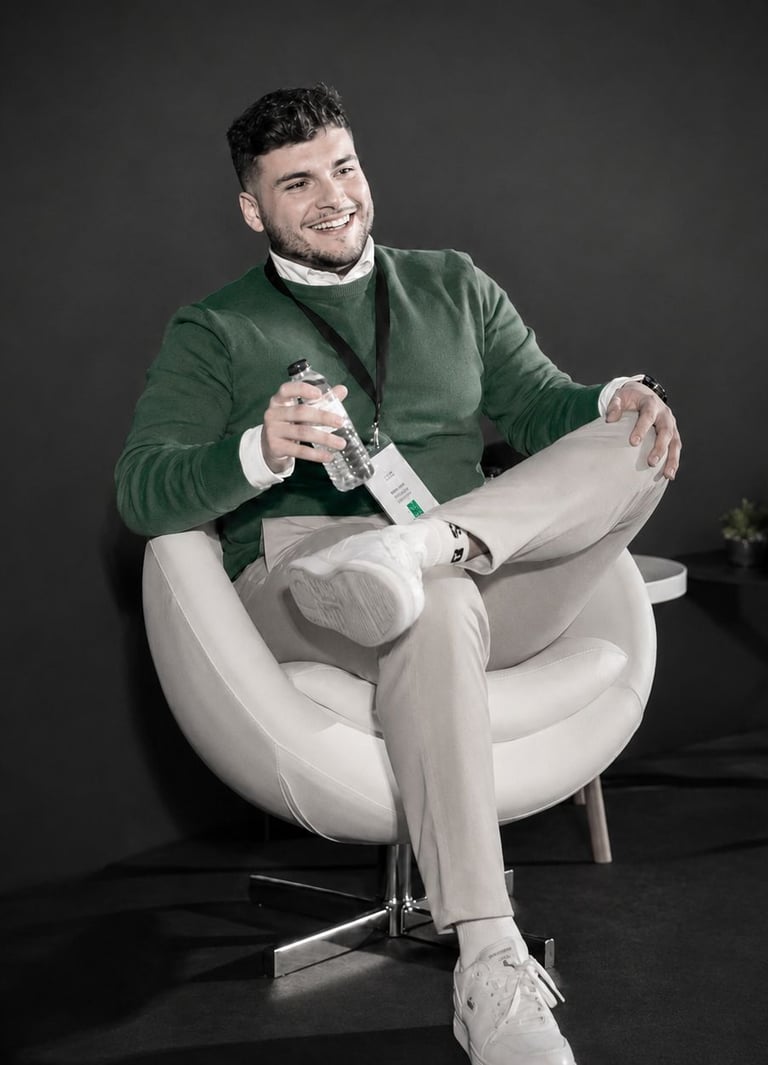 Smiling man in a green sweater sitting on a white swivel chair at a professional event conference.