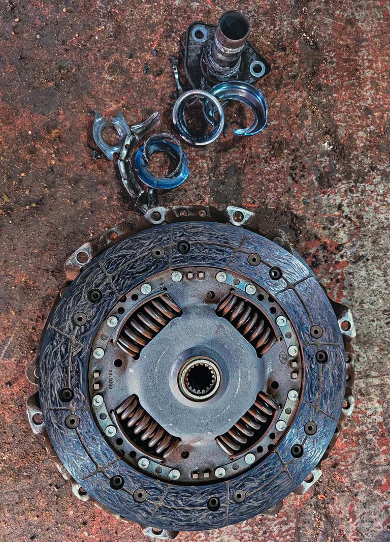 Damaged car clutch plate and broken metal release bearing on a dirty garage floor.