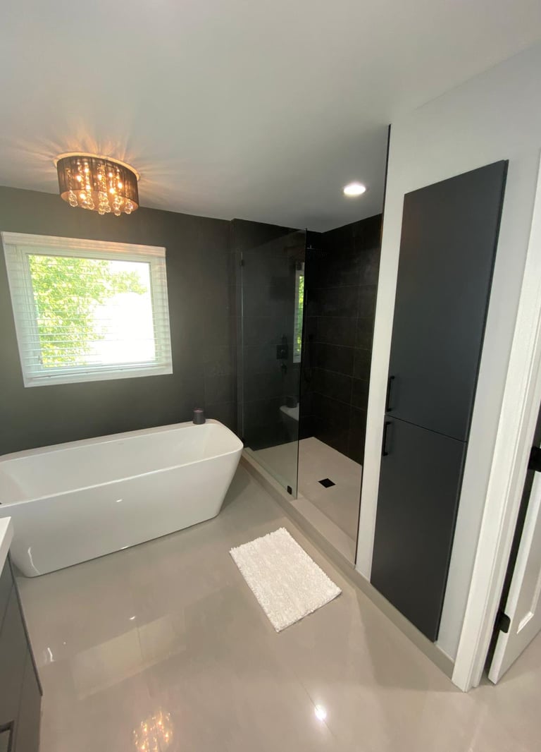 Modern master bathroom featuring a white freestanding bathtub and a glass walk-in shower with dark tiles.
