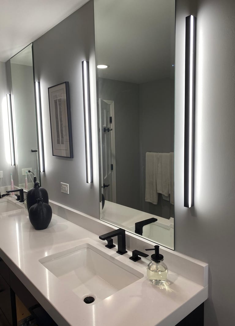 Modern bathroom vanity with white quartz countertop, black faucets, and vertical LED wall sconces beside mirrors.