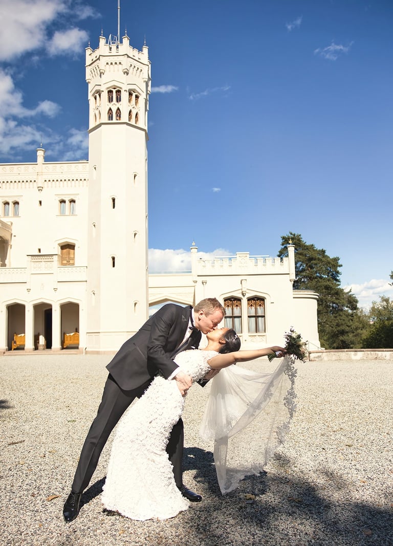 En brud og brudgom som kysser foran et slott.