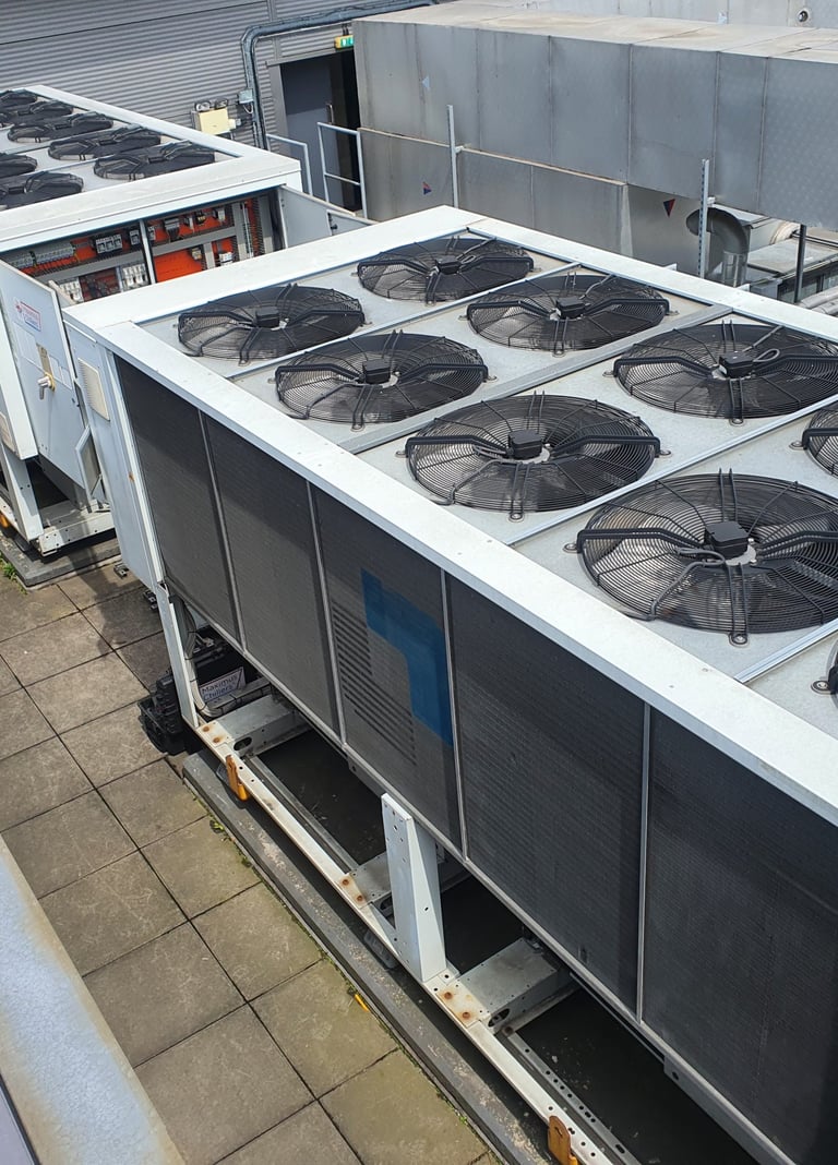 Large industrial HVAC chiller units with exhaust fans installed on a commercial building rooftop.
