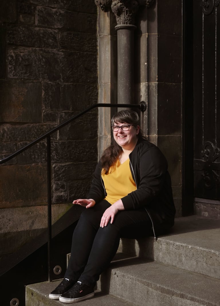 Laura is sitting on stone steps looking just off camera smiling at the sunshine