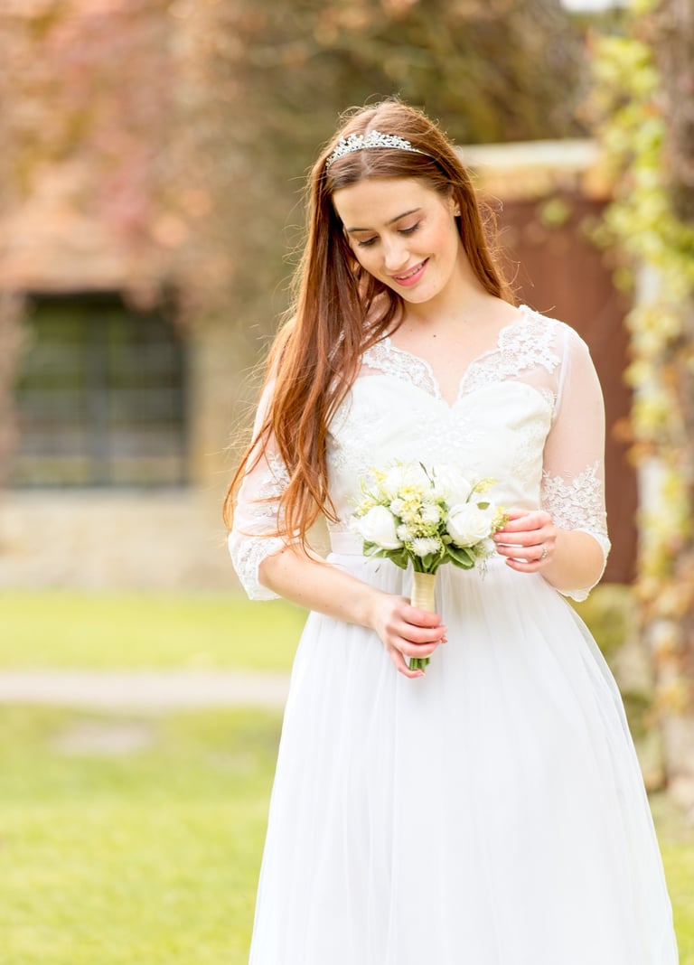 bride in white dress, backlight, blurry autumn leaves background, bride holding bouquet and looking at bouquet