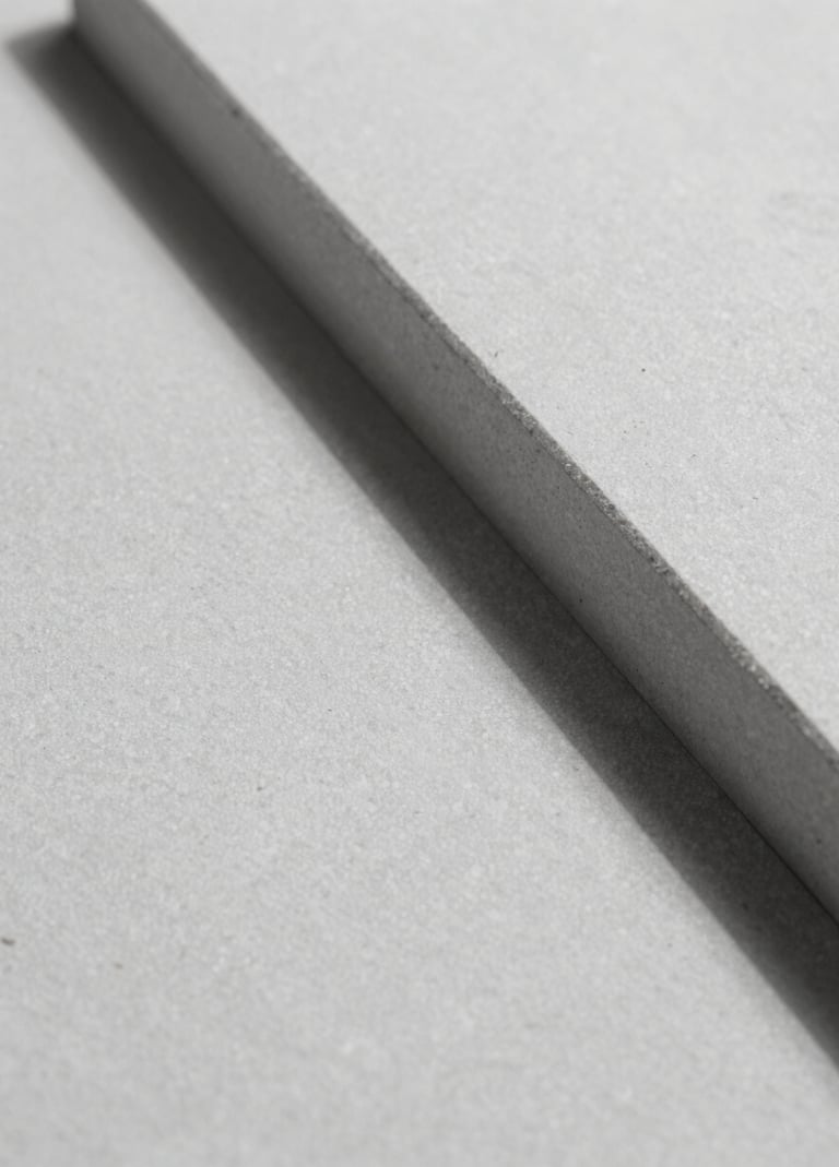 A minimalist macro shot of architectural material, likely smooth light grey stone or textured plaster, with a sharp diagonal shadow cutting across it. High contrast, high-end feel using #F9F7F2 and #333333 tones.