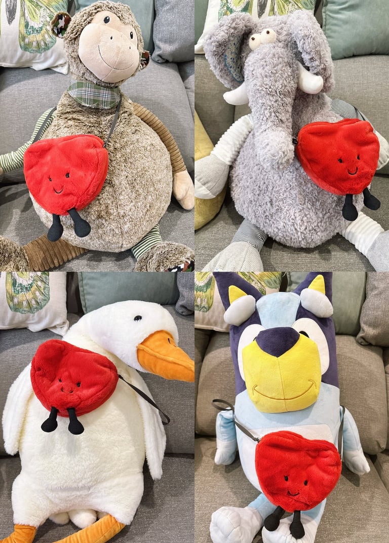 Four plush stuffed animals wearing a red heart-shaped crossbody bag with a smiley face.