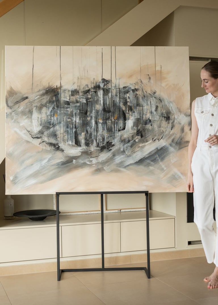 A woman in a white jumpsuit stands next to a large abstract expressionist painting in a modern home.