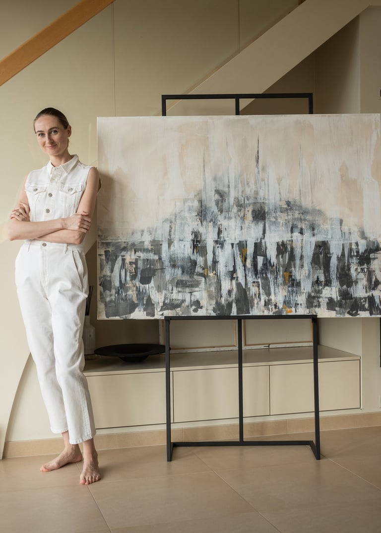 A female artist in white denim posing next to her large abstract painting on an easel.