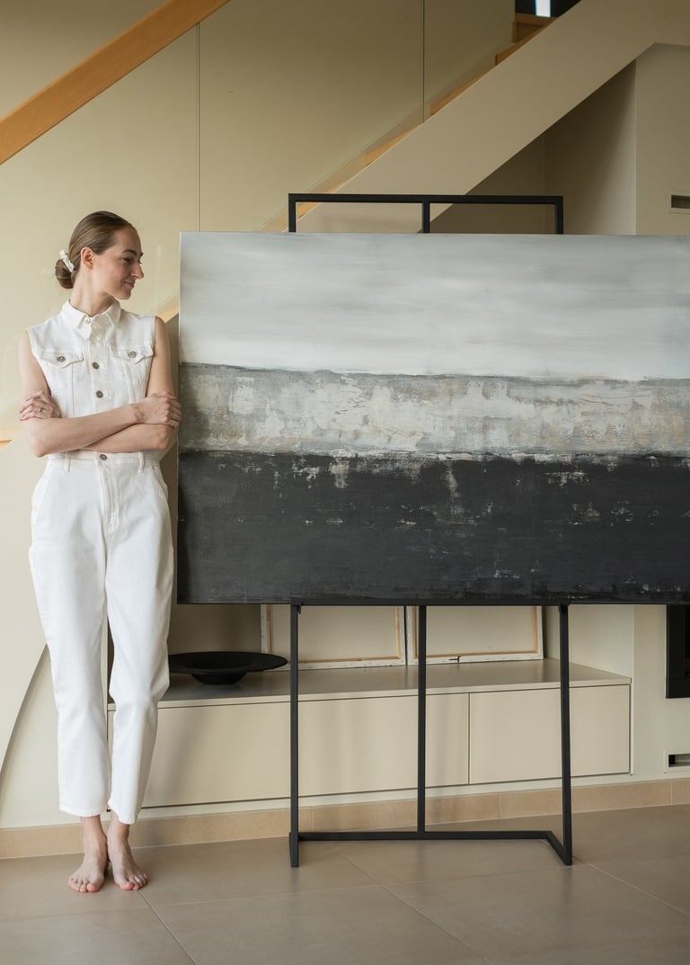 Artist standing by large abstract landscape painting on an easel in a modern minimalist living room.