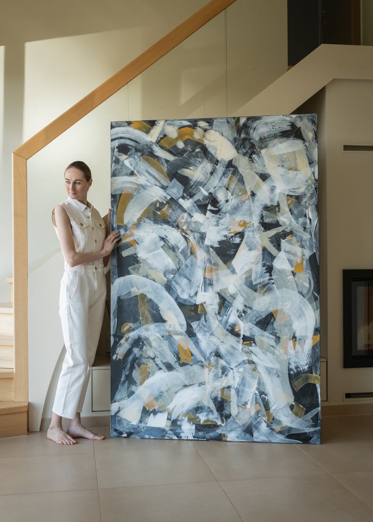 Artist standing next to a large abstract expressionist painting featuring black, white, and gold brushstrokes.