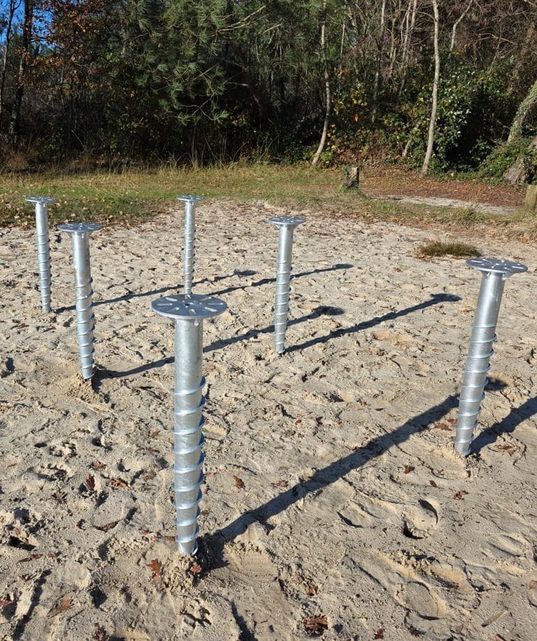Plusieurs pieux vissés installés dans le sable pour un chalet bois