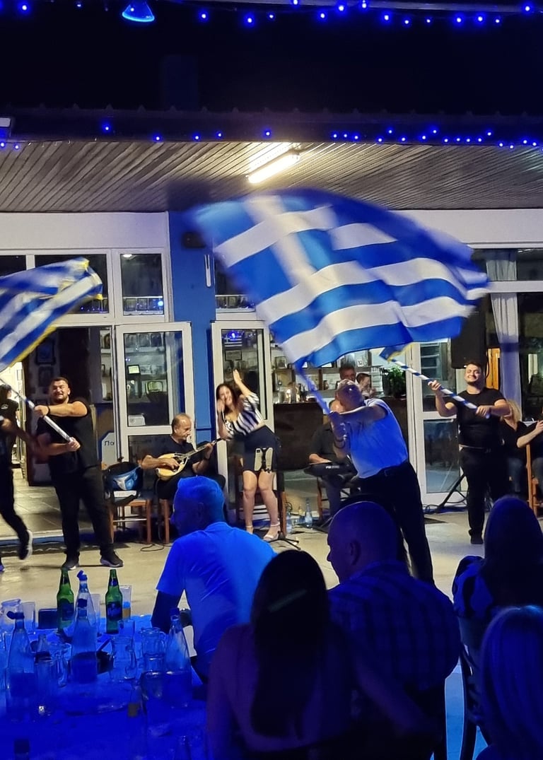 Greek dancers waving flags at a traditional night festival with live bouzouki music.