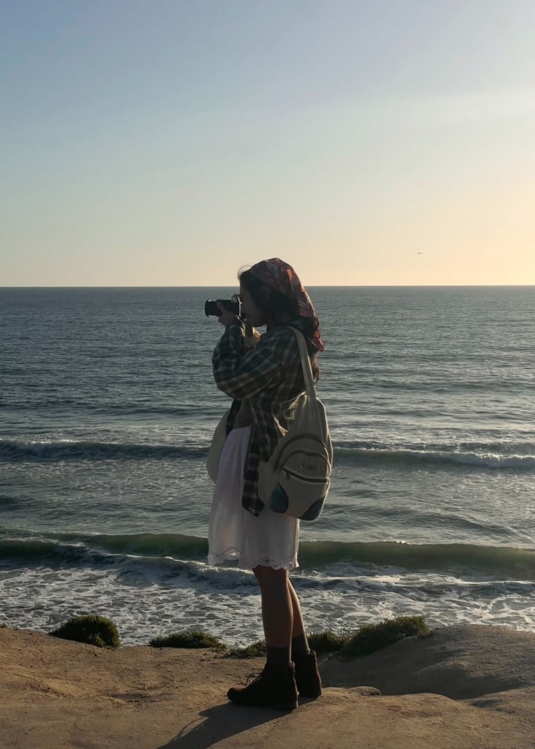 Vibey full body candid shot of me holding camera up to my face, standing on cliffs over ocean.Earthy