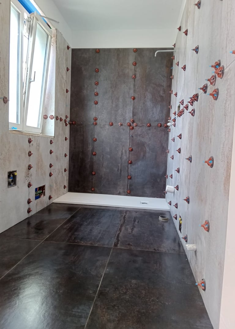Bathroom renovation featuring dark floor tiles and wall tiling with red leveling spacers.