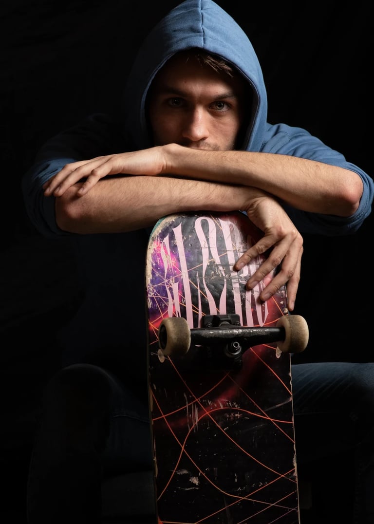 Un jeune homme vêtu d'un sweat à capuche bleu, assis avec un skateboard entre les bras