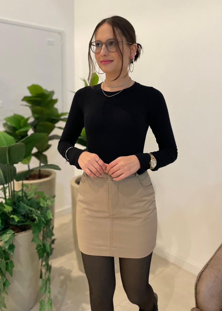 Mulher vestindo saia curta de sarja bege com bolsos frontais e blusa preta de manga longa.