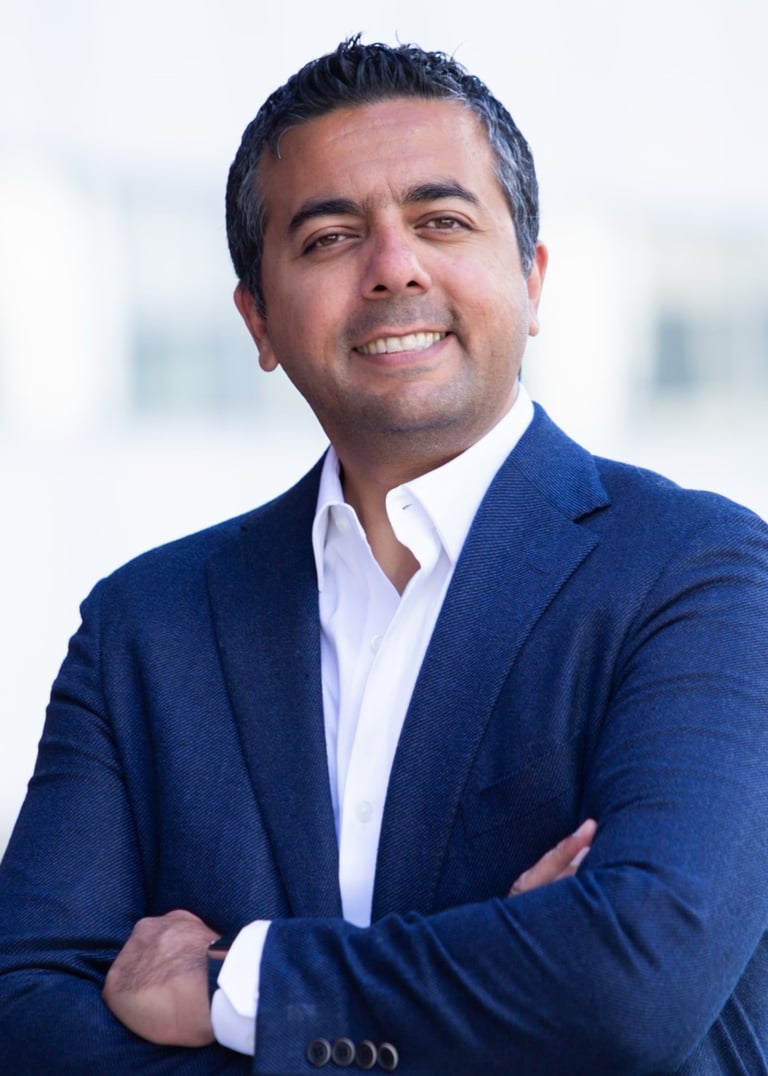 Professional portrait of a smiling businessman in a blue blazer and white shirt with arms crossed.