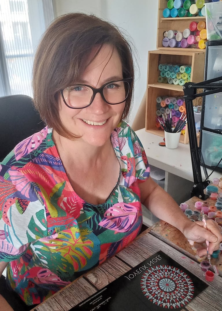 a woman sitting at a table painting dot mandala
