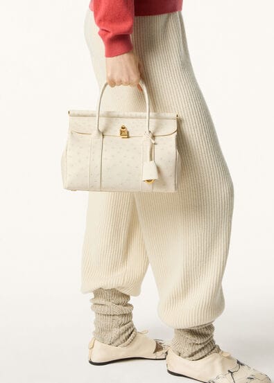Cream outfit holding structured leather handbag.