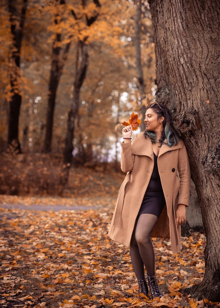 a woman in a coat and boots standing in front of a tree
