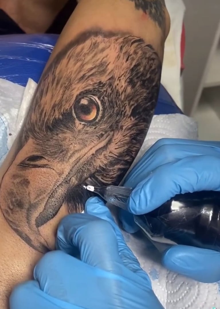 Detailed black and grey realism bald eagle tattoo being inked on a forearm by a professional artist.