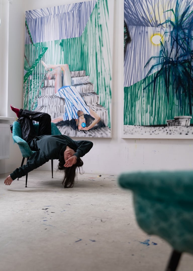 Artist posing upside down in a teal chair in front of large abstract contemporary paintings in a studio.