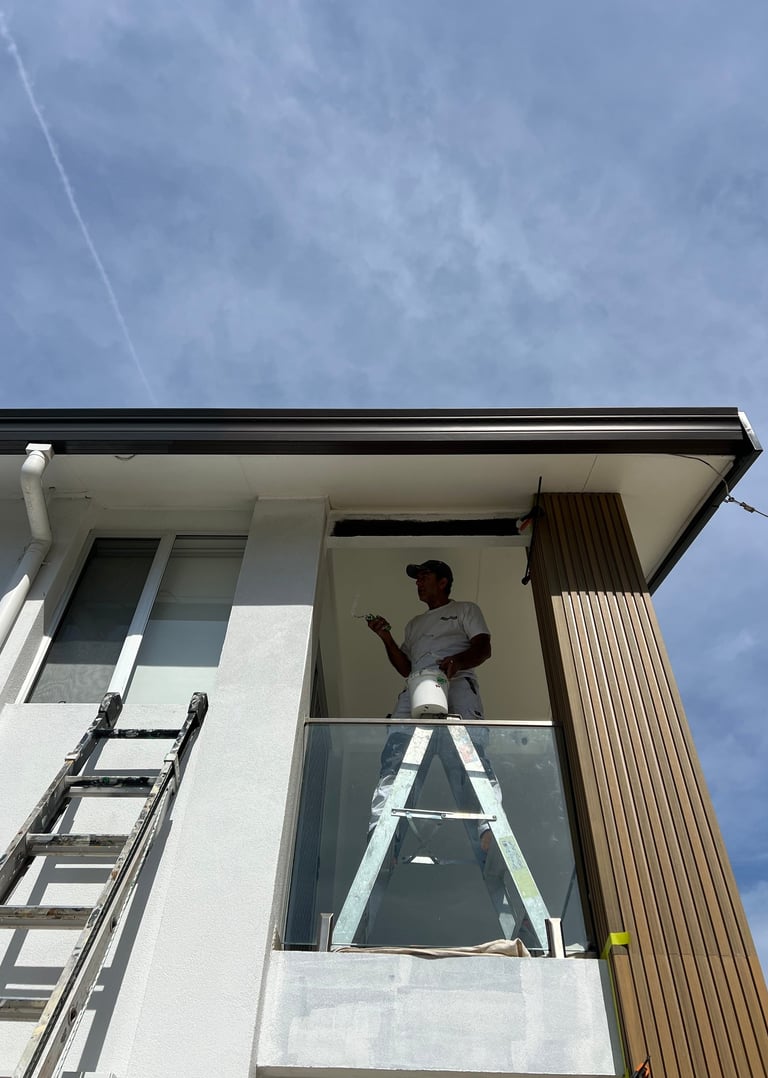 Painter in oster bay on  ladder to reach up to a window