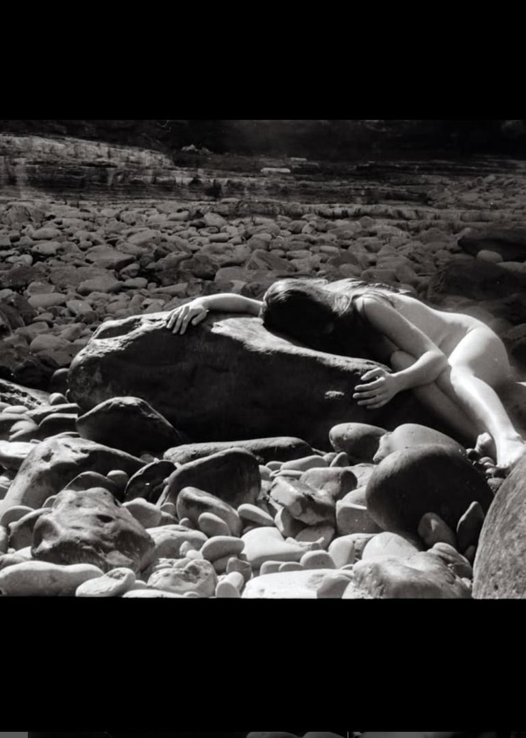 A woman holding and being held by smooth solid rocks surrounded by smaller rock fragments