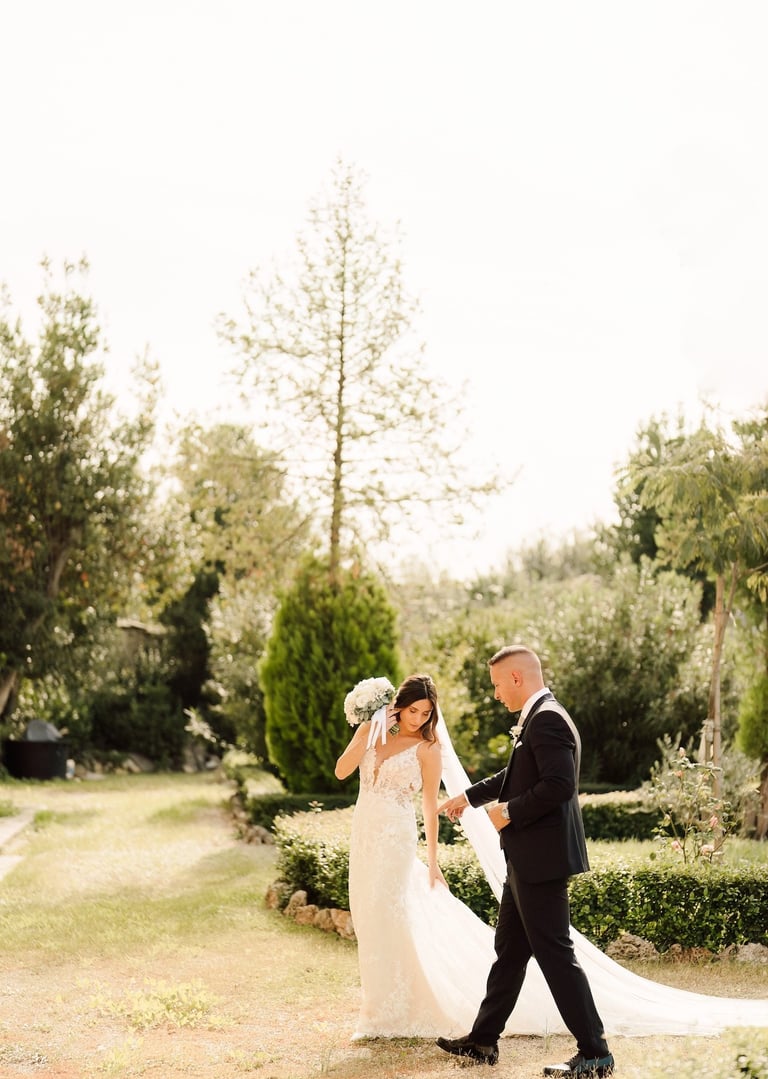 Un'elegante sposa in abito da sposa di pizzo e lo sposo in smoking nero passeggiano in un rigoglioso