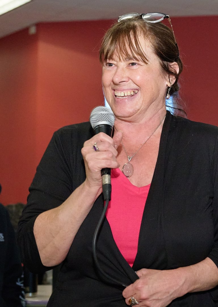 a woman in a black jacket is holding a microphone and smiling