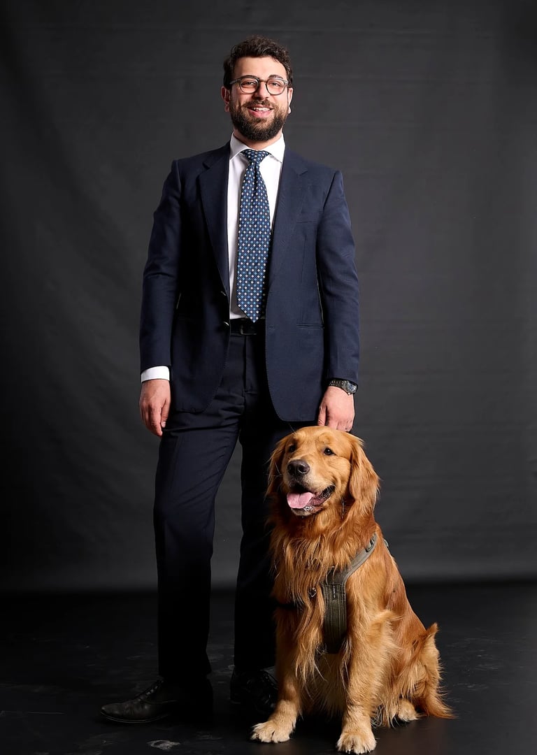 A man in a navy blue suit and tie posing with his golden retriever dog against a dark studio background.