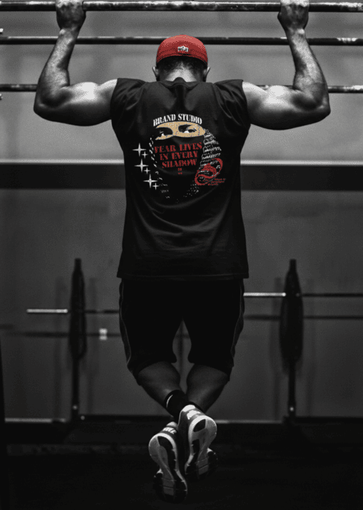 Atleta musculoso con camisa sin mangas negra con estampado gráfico realizando dominadas en un gym.