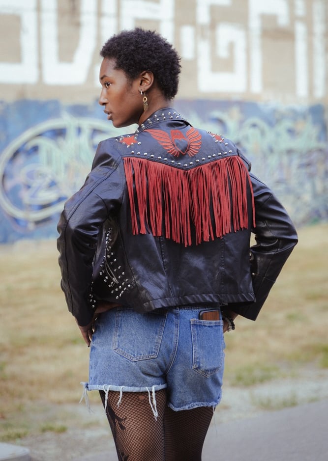 Fuller image of model looking over her shoulder, cool earrings and black denim jacket.