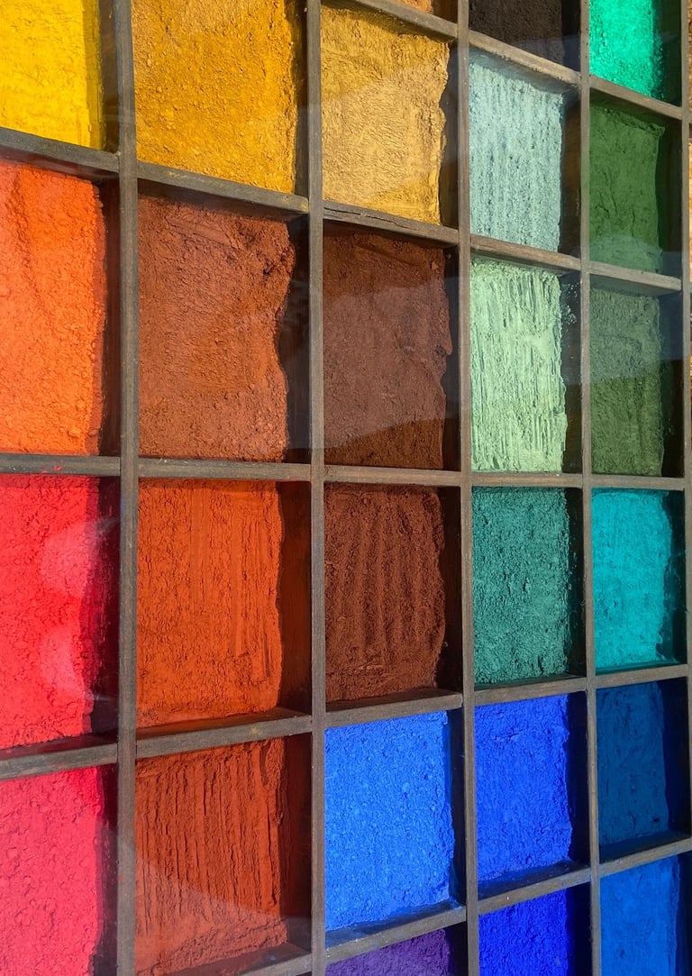 A wooden display case featuring vibrant rows of colorful artist pigment powders in a variety of hues.