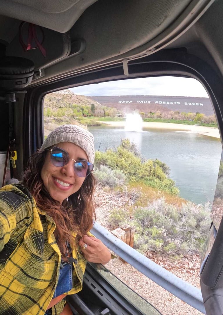 Mujer sonriente con camisa de franela amarilla tomándose una selfie desde una camper van con vista a