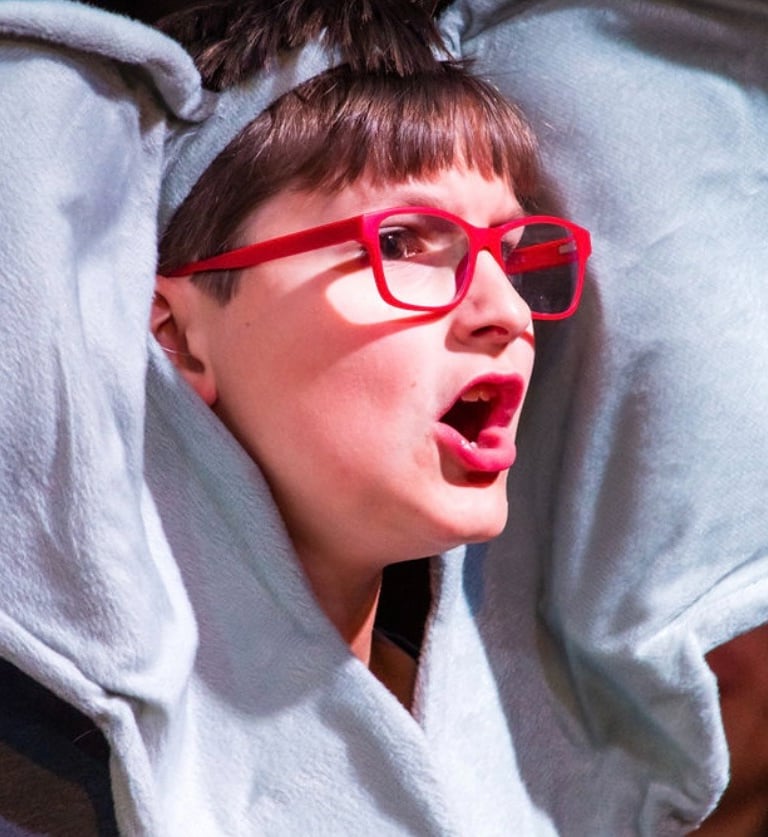 Child wearing an elephant costume with large ears and red glasses, performing expressively on stage