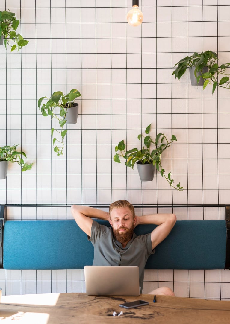 Persona tomando una pausa mental frente a su laptop en un espacio de trabajo con plantas