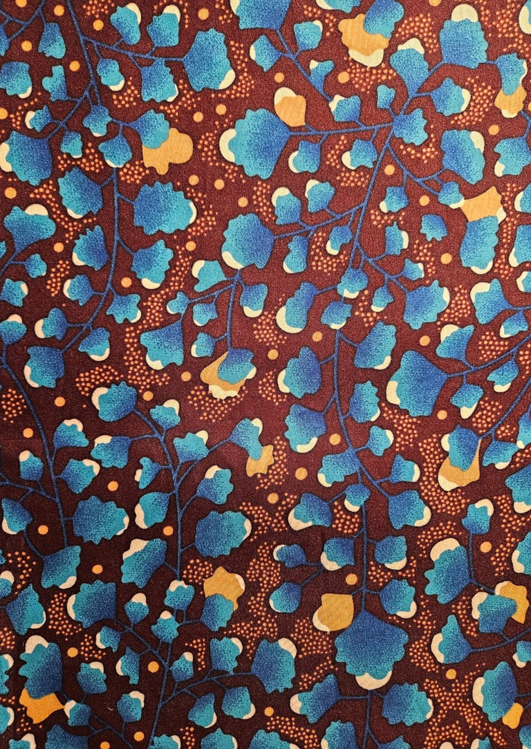 Floral African wax print fabric with blue leaf patterns and orange accents on a dark brown background.