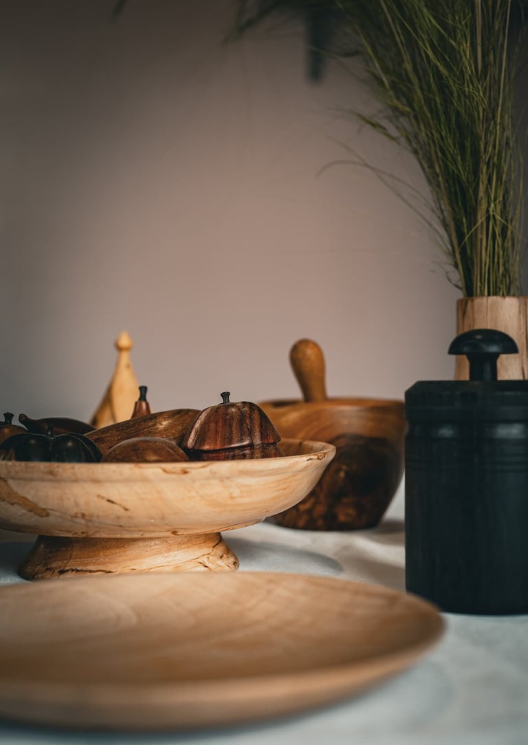 Objets artisanaux en bois posés sur une table : plat en bois clair sur pied rempli de fruits décorat