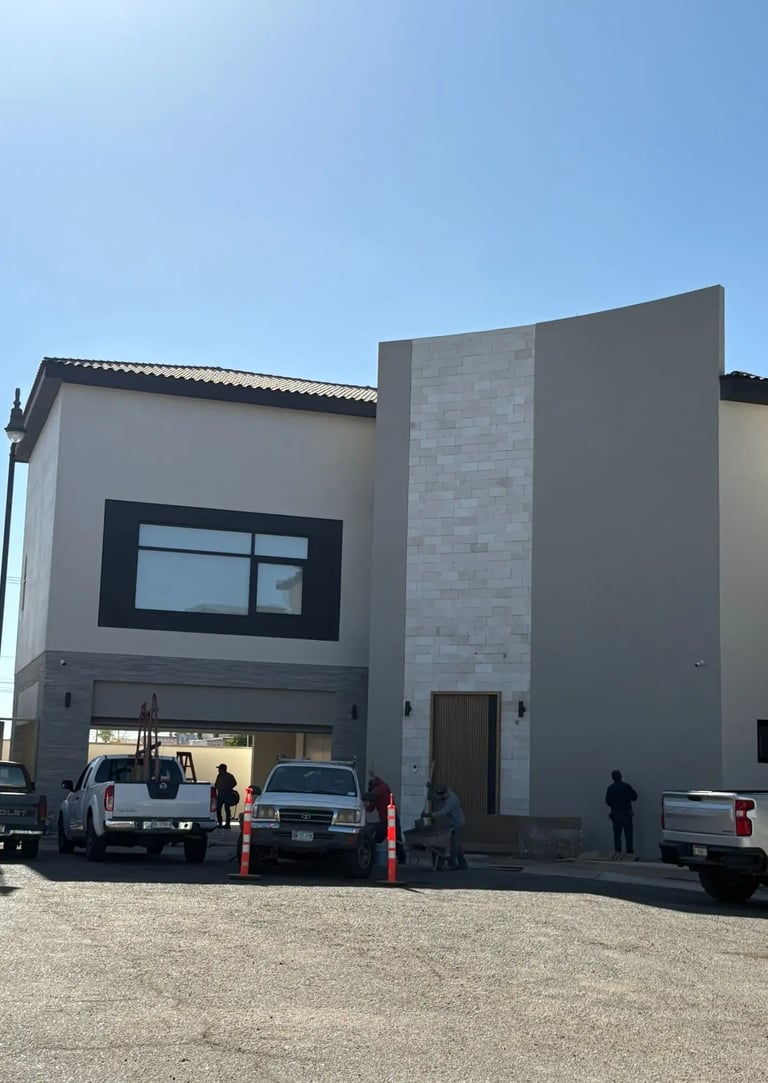 Casa moderna de dos pisos en construcción, con trabajadores y vehículos en el exterior