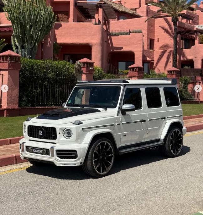 White Brabus Mercedes G-Wagon luxury SUV parked in front of pink Mediterranean villas for rent.