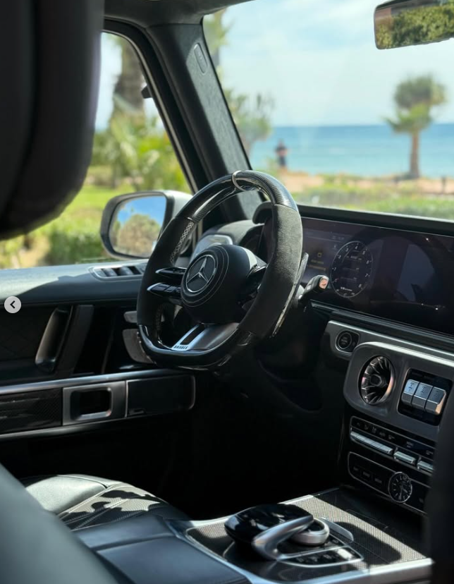 Luxury Mercedes-Benz G-Wagon interior with a carbon fiber steering wheel parked by the ocean.